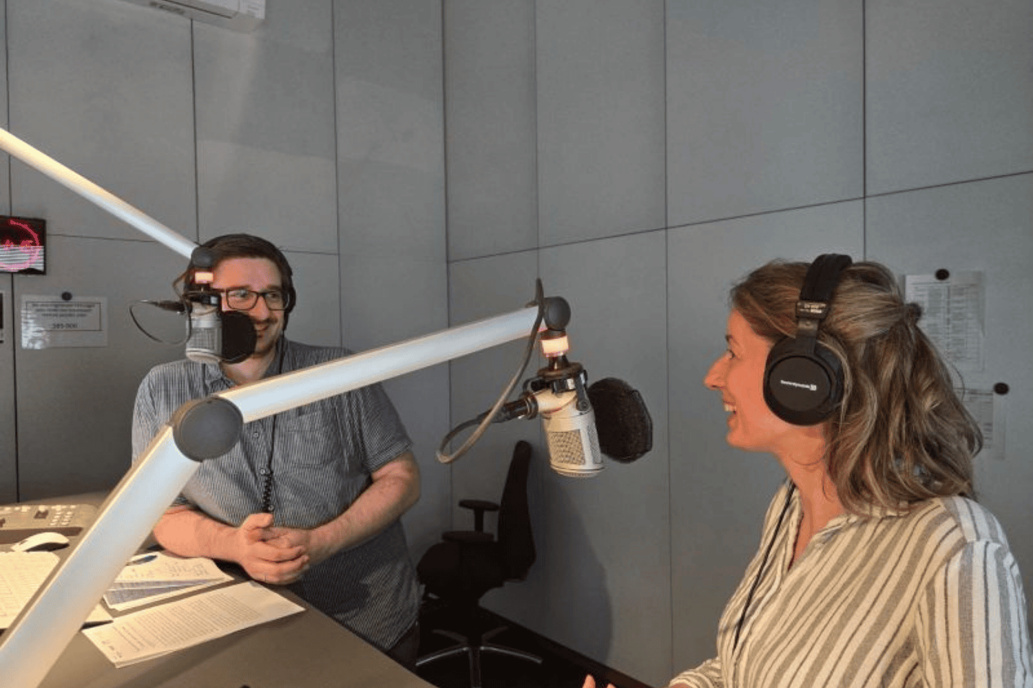 Zwei Personen mit Kopfhörern führen ein Interview in einem Radiostudio, beide sprechen in Studiomikrofone.
