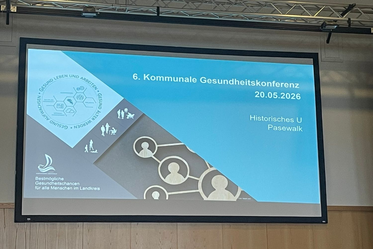 Ein Präsentationsbildschirm im Historischen U Pasewalk mit der Titelfolie der „6. Kommunalen Gesundheitskonferenz“ am 20.05.2026. Auf der Folie sind Logos und grafische Symbole zu Gesundheit, Vernetzung und gesellschaftlicher Teilhabe zu sehen. Links unten steht der Slogan „Bestmögliche Gesundheitschancen für alle Menschen im Landkreis“.
