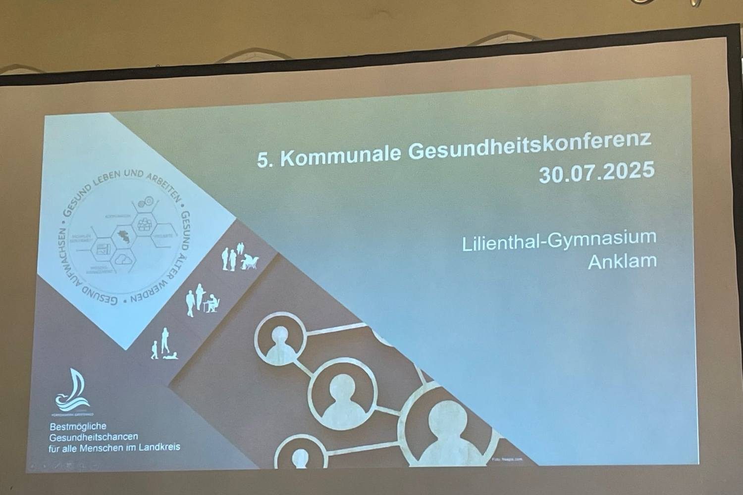 Große Präsentationsfolie zur „5. Kommunalen Gesundheitskonferenz“ am 30.07.2025 im Lilienthal-Gymnasium Anklam. Die Folie zeigt grafische Elemente zu Gesundheit, Arbeit und Lebensumfeld sowie den Slogan „Bestmögliche Gesundheitschancen für alle Menschen im Landkreis“.