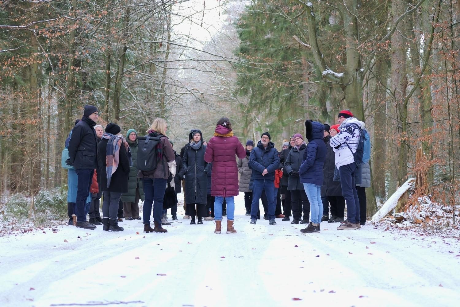 Gruppe von etwa 20 Personen bei einer Exkursion während der Zwischenbegutachtung der One-Health-Region Vorpommern, stehend auf einem verschneiten Waldweg und im Gespräch miteinander.